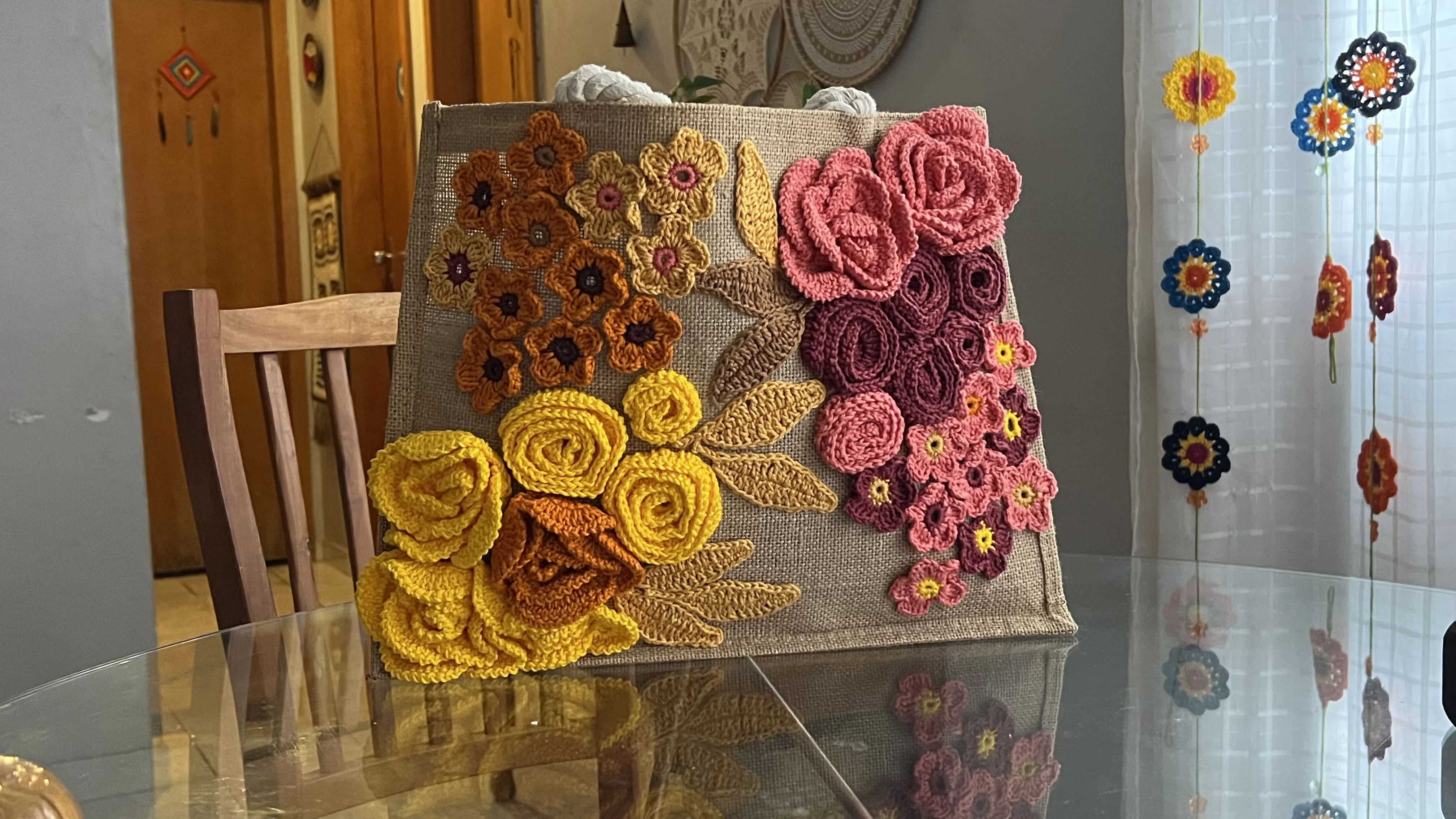 Bolsa de juta com flores em crochê sobre mesa de vidro - ângulo frontal
