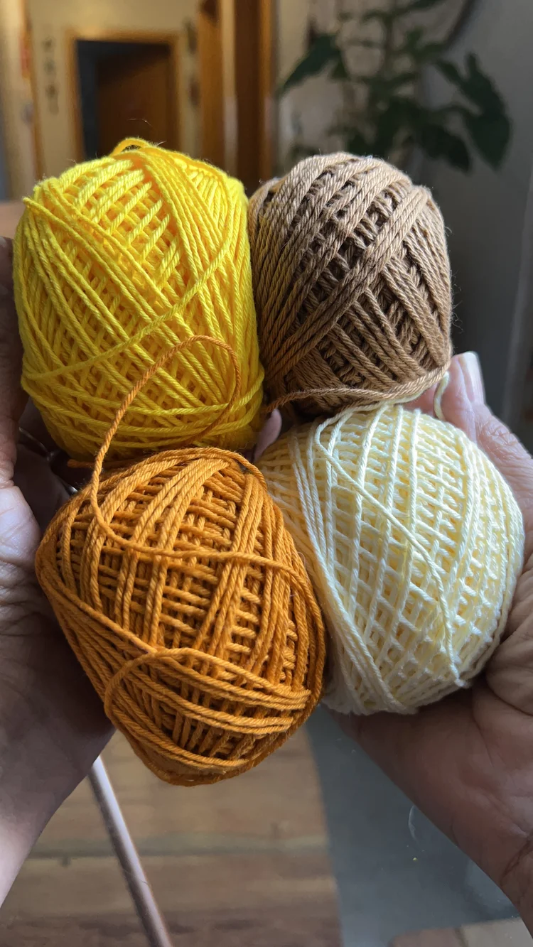 Bolsa finalizada apoiada com novelos de linha nas cores caramelo, amarelo e off-white
