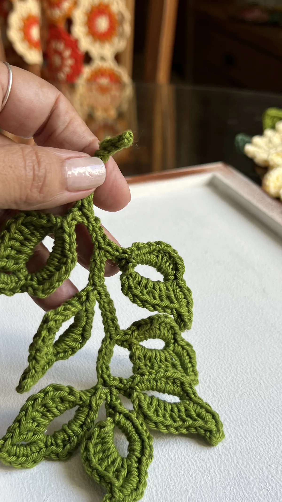 Ramo de folhas de crochê verde na mão, mostrando o tamanho da peça